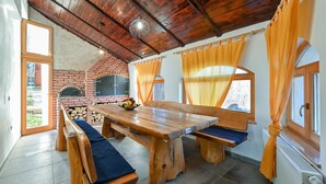 A rustic kitchen with a brick oven, wooden benches, and a large table.