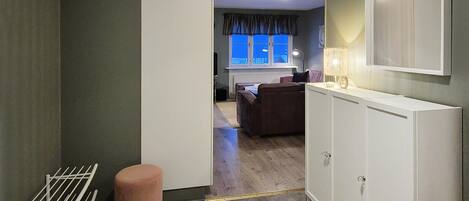 A hallway with a radiator, a pink stool, and a white cabinet.