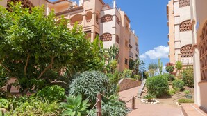 A courtyard with a paved walkway surrounded by lush greenery and buildings with traditional architecture. - Mijas Golf Boutique Apartment - Golf & Leisure (Mijas)