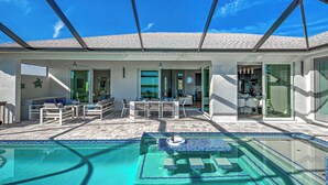 A covered outdoor pool area with a patio, seating, and a small fire feature. - Casa Riva | Lagoon Front | 2 Masters | Pool | Spa | Swim up Bar | Lounge (Port Charlotte)
