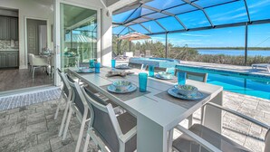 A dining area with a view of a swimming pool and a beach. - Casa Riva | Lagoon Front | 2 Masters | Pool | Spa | Swim up Bar | Lounge (Port Charlotte)