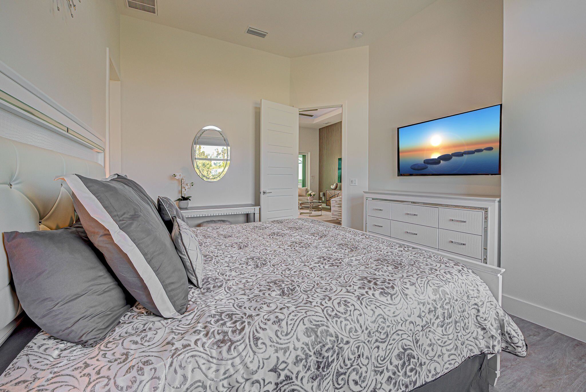 A bedroom with a large bed, a television mounted on the wall, and a view of the outdoors through a window.