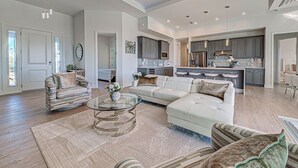 A spacious living room with a large sectional sofa, a glass coffee table, and a striped armchair. - Casa Riva | Lagoon Front | 2 Masters | Pool | Spa | Swim up Bar | Lounge (Port Charlotte)