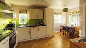 A compact kitchen with a stove, microwave, and a dining area with a table and chairs. - An idyllic Countryside Cottage Stay, near the Sea (Nolton Haven)