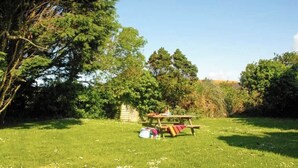 A grassy area with a wooden picnic table and benches, surrounded by trees and a small shed. - An idyllic Countryside Cottage Stay, near the Sea (Nolton Haven)