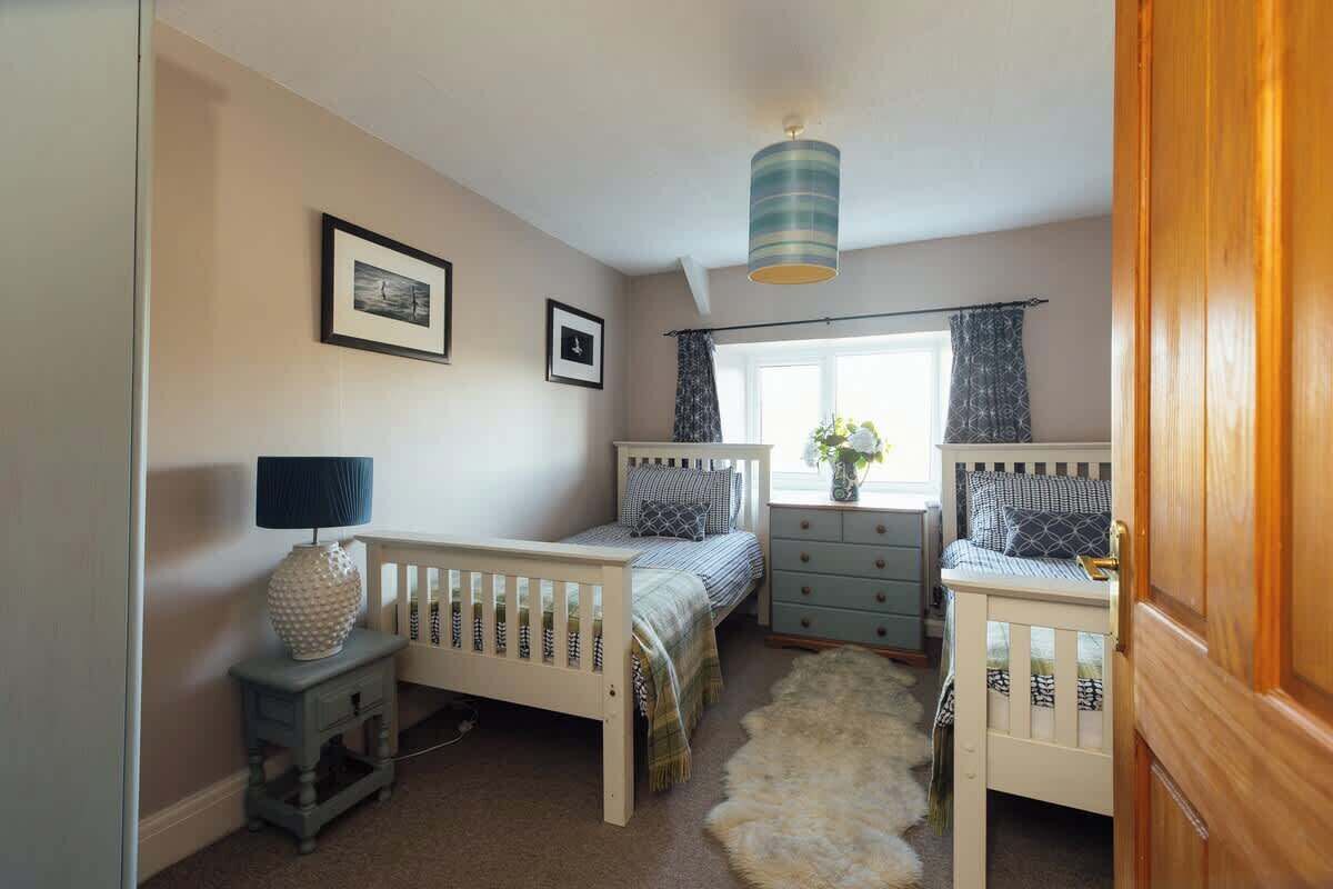 A bedroom with two single beds, a dresser, a lamp, and a window with curtains.