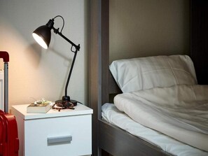 A neatly made bed with white bedding, a bedside table with a lamp, and a red suitcase. - 8 Person Holiday Park Home in Goteborg (Gothenburg)