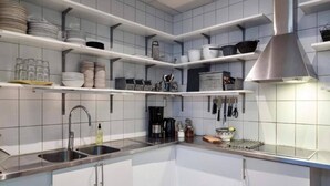 Una cucina moderna con mobili bianchi, piani di lavoro in acciaio inossidabile e diversi utensili da cucina sugli scaffali.