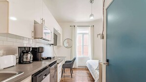 A compact kitchen with modern appliances, a dining area with a chair, and a bedroom with a bed and window. - Mont-Royal Ave Studio · Walk to La Fontaine Park (Montreal)