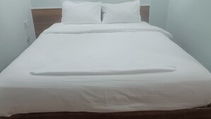 A single bed with white bedding in a room with light-colored walls and a wooden floor.