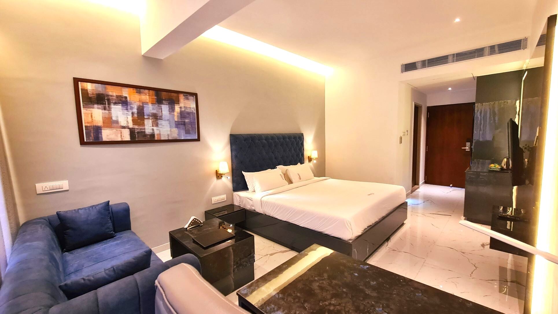 A hotel room with a bed, a sofa, a coffee table, a painting, and a large mirror.