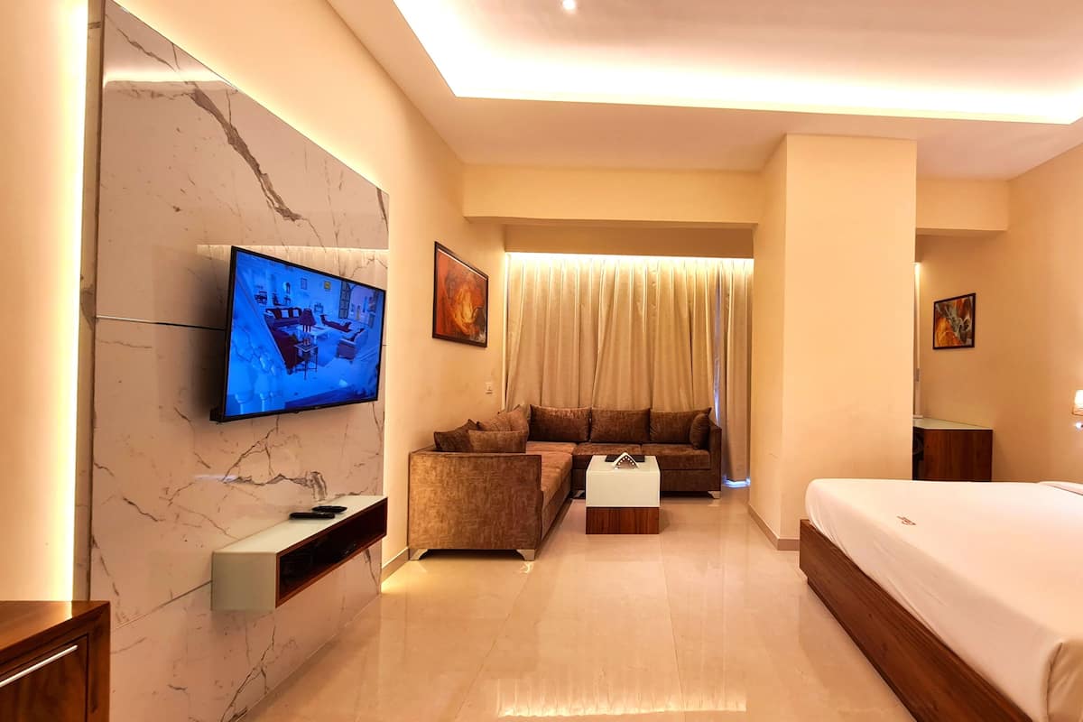 A hotel room with a large bed, a sofa, a TV mounted on a marble wall, and a curtain-covered window.