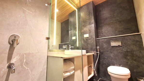 A modern bathroom with a marble floor, a glass shower enclosure, a white toilet, and a vanity with a mirror. - Galaxy Club & Hotel (Bijapur)