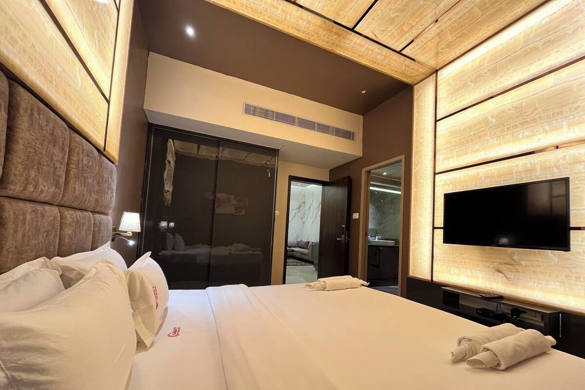 A hotel room with a large bed, a flat-screen TV mounted on the wall, and a wooden headboard.