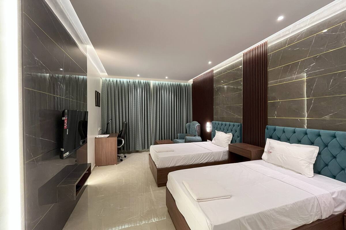 A modern hotel room with two beds, a desk, a chair, and a television.