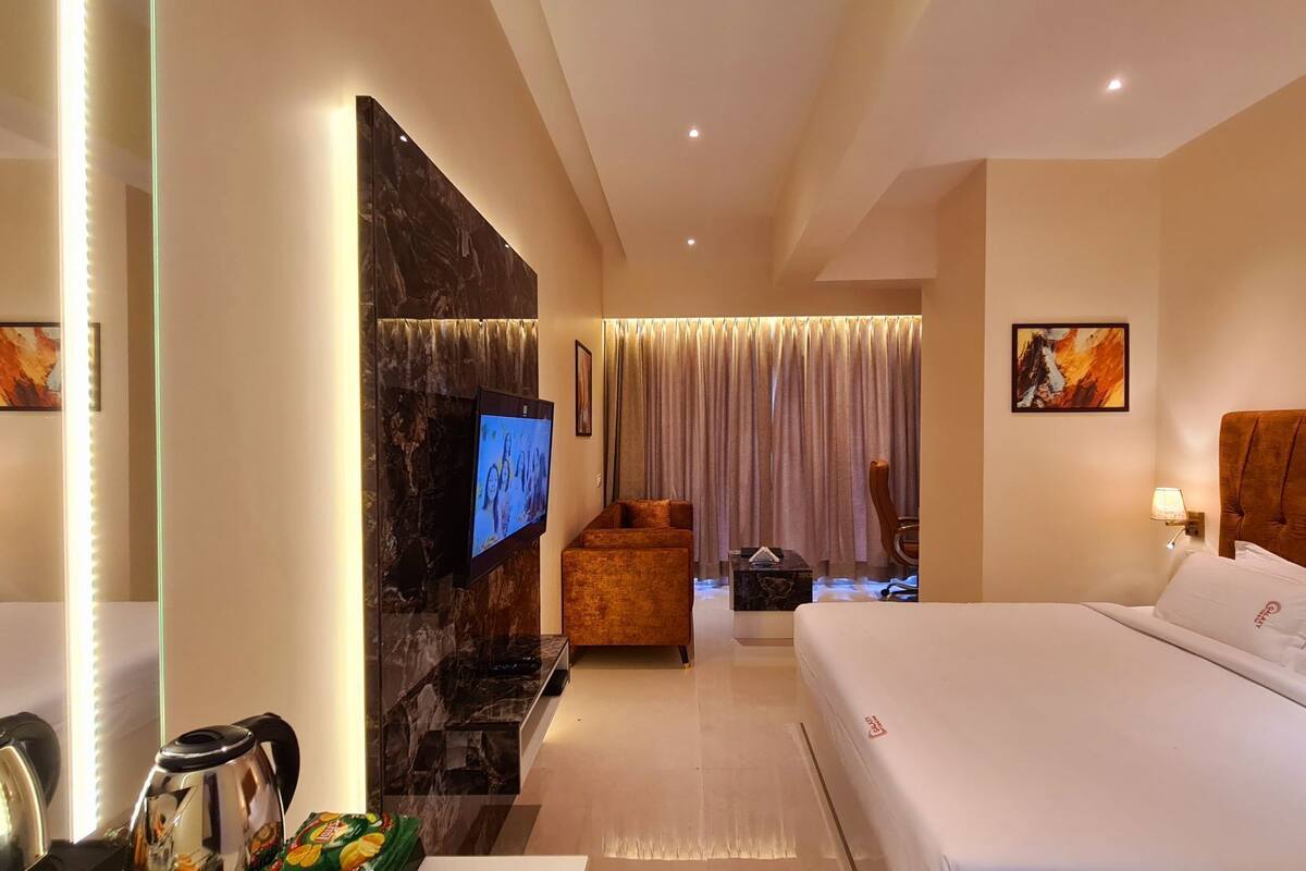 A hotel room with a large flat-screen TV, a sofa, a bed, and a dining table.