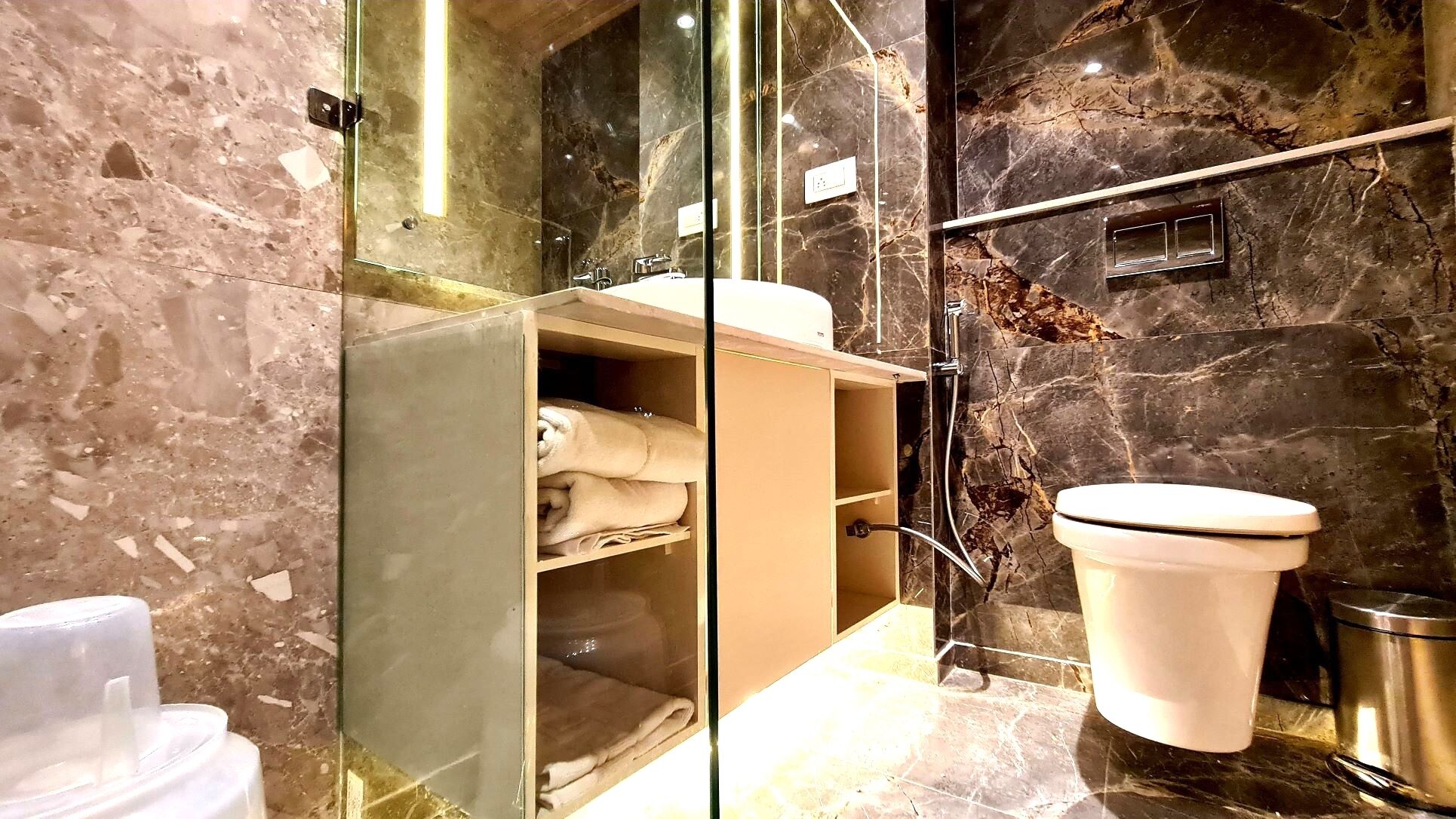 A modern bathroom with a glass-enclosed shower, marble walls, and a toilet.