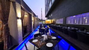 Un espacio exterior estrecho para comer con mesas y sillas, iluminado con luces azules.