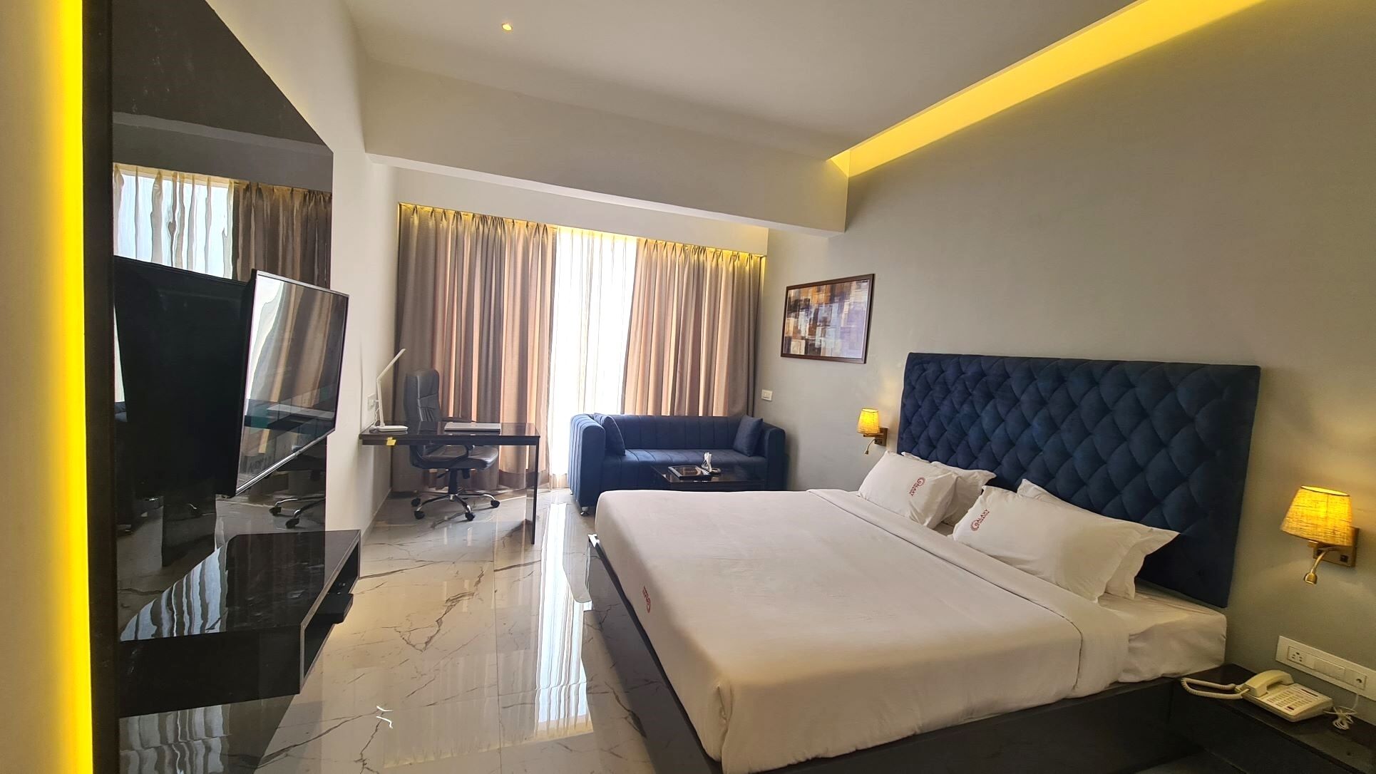 A hotel room with a large bed, a desk with a computer, a TV, and a sofa.