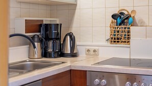 Una cocina con cafetera, hervidor y un cesto de utensilios.