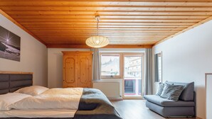 Un dormitorio con cama, sofá, techo de madera y ventana con vista a edificios.