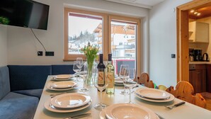 Un comedor con una mesa dispuesta para cuatro, un televisor montado en la pared y vistas a edificios a través del ventanal.