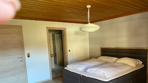 Una camera da letto con un letto, pavimento in legno, soffitto in legno e zona doccia.