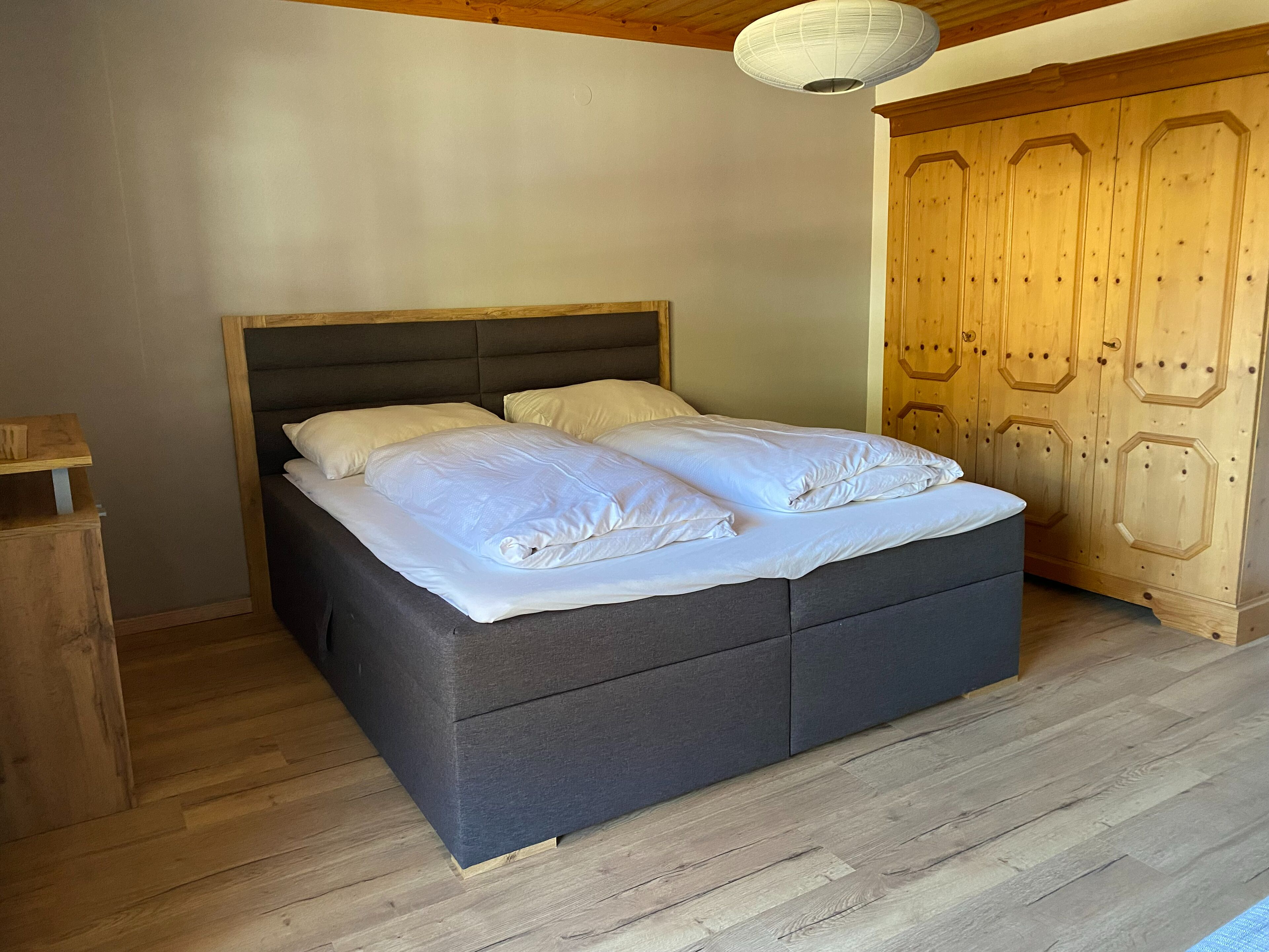 A bed with a dark headboard, white bedding, and a wooden wardrobe with a hexagonal design.