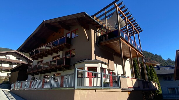 Un edificio a più piani con balconi, una facciata in legno e un cielo azzurro sullo sfondo.