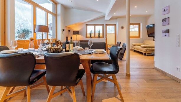 Een moderne eetruimte met een houten tafel, zwarte stoelen en uitzicht op het groen door grote ramen.