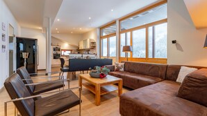 Una sala de estar moderna con un sofá de cuero marrón, una mesa de centro de madera y un comedor con una silla negra y una mesa.