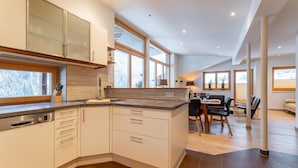 Una cocina moderna con armarios blancos, un lavavajillas Bosch y un comedor con mesa y sillas.