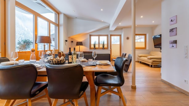 Un comedor moderno con una mesa de madera, sillas negras y vistas al exterior a través de amplios ventanales.