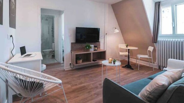 Un salon moderne avec un canapé, un fauteuil blanc, une petite table, un téléviseur et une bibliothèque.