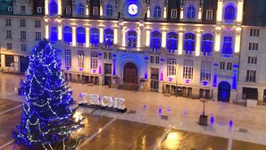 Un bâtiment historique doté d’une tour horlogée, de fenêtres illuminées et d’un sapin de Noël.