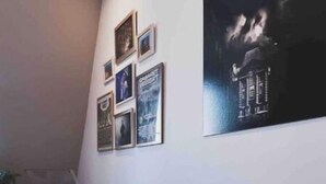 Un salon avec un canapé de couleur sombre, plusieurs coussins et un mur décoré de tableaux encadrés et d’une grande peinture abstraite.
