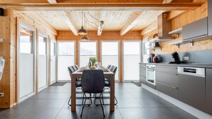 A modern kitchen with wooden beams, a dining area with a table and chairs, and large windows.