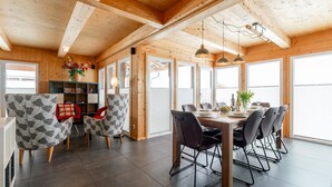 A wooden interior with a dining area, chairs, a table, and a bookshelf.