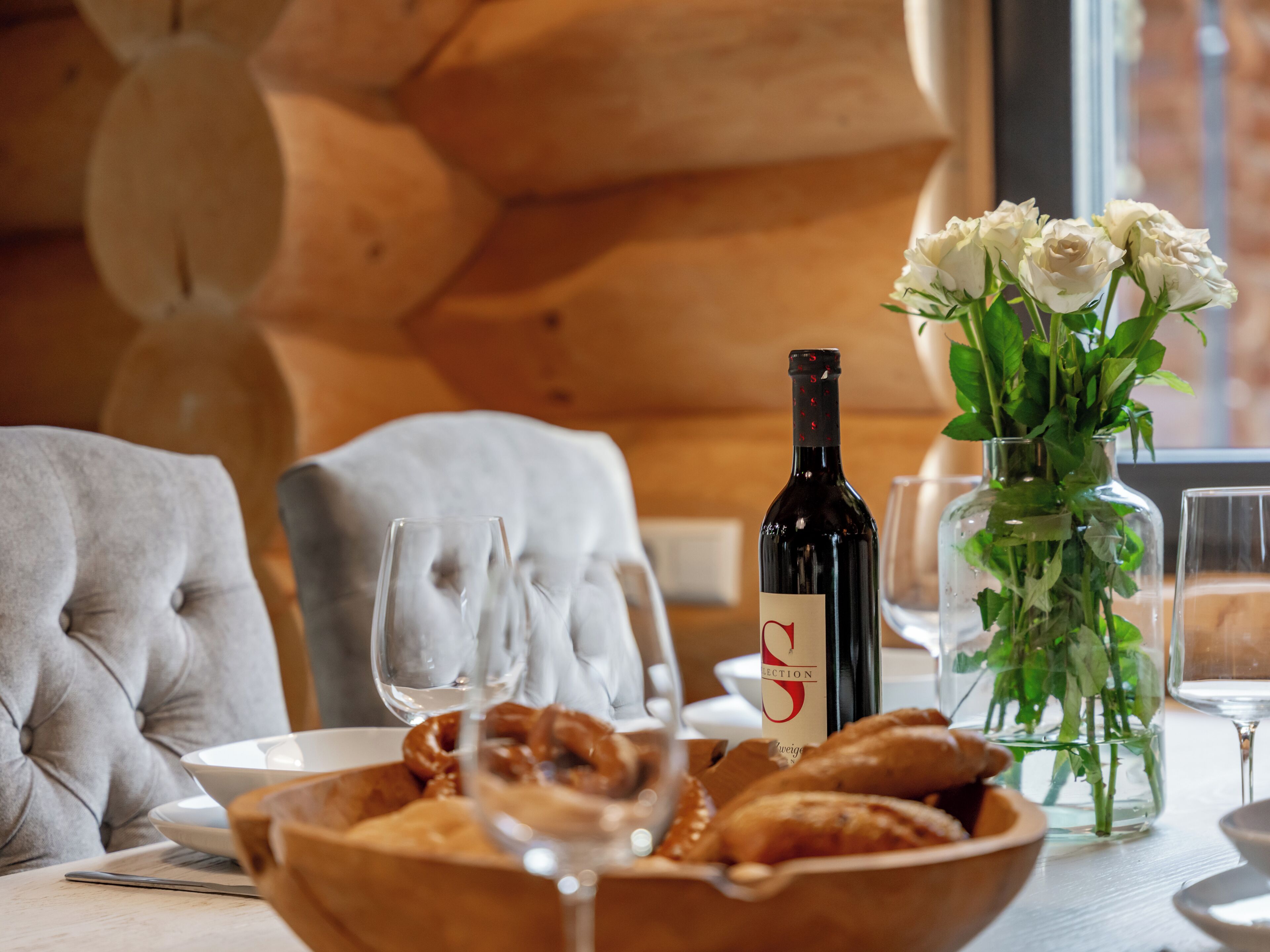 Una mesa de comedor con una botella de vino, un bol de pretzels y un jarrón de flores blancas.
