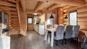 A log cabin interior with a dining area, kitchen, and a staircase leading to another level.