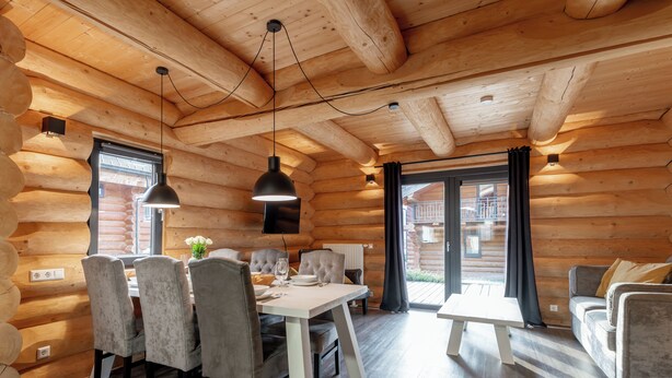 A log cabin interior with a dining area, sofa, and a large window.
