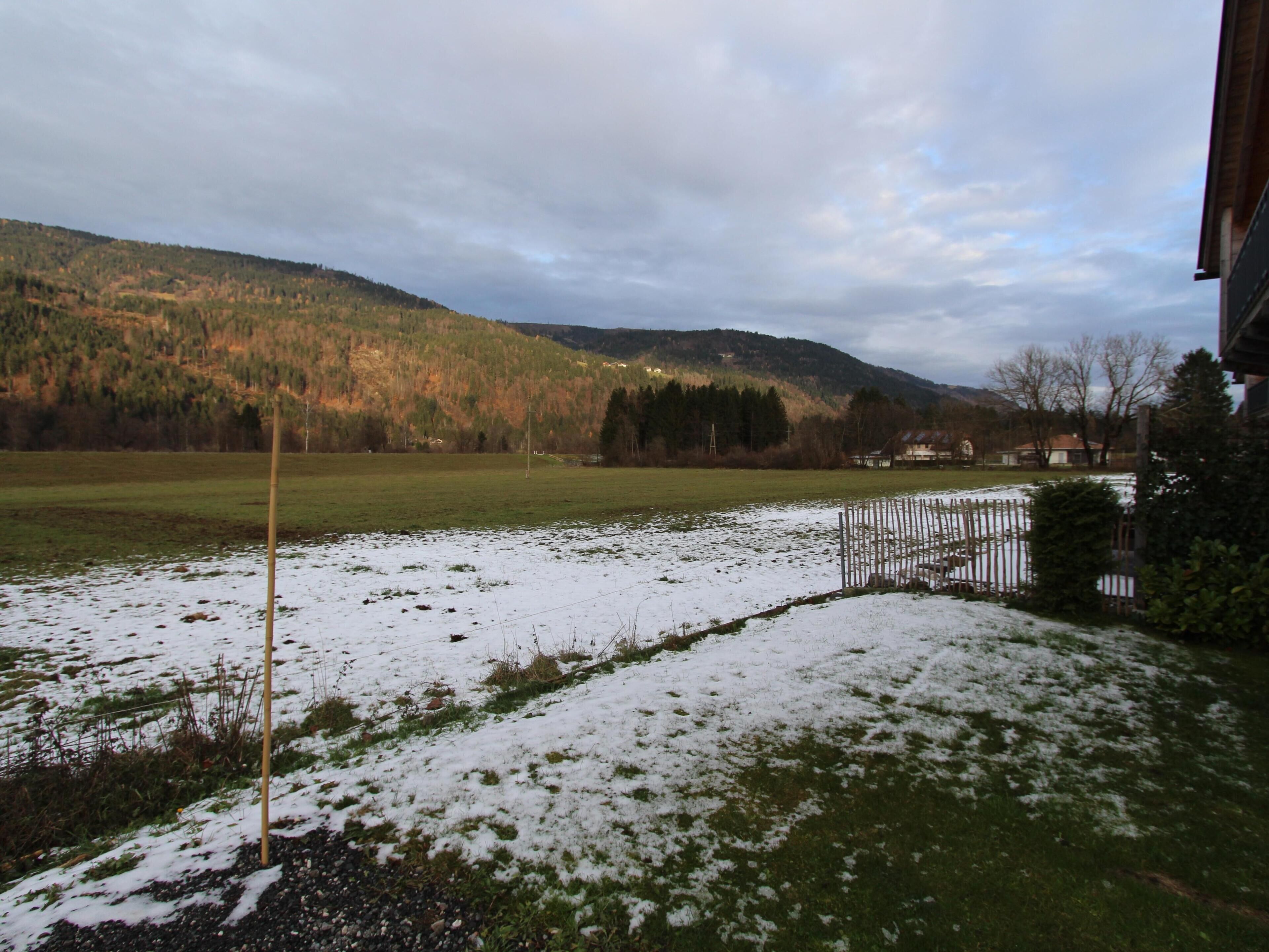 Ein mit Schnee bedecktes Feld mit einem Holzzaun und einem Gebäude im Hintergrund.