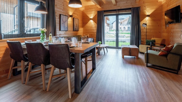 Ein Holzblockbau-Innenraum mit Essbereich, Sitzgelegenheiten und Blick durch Glastüren.