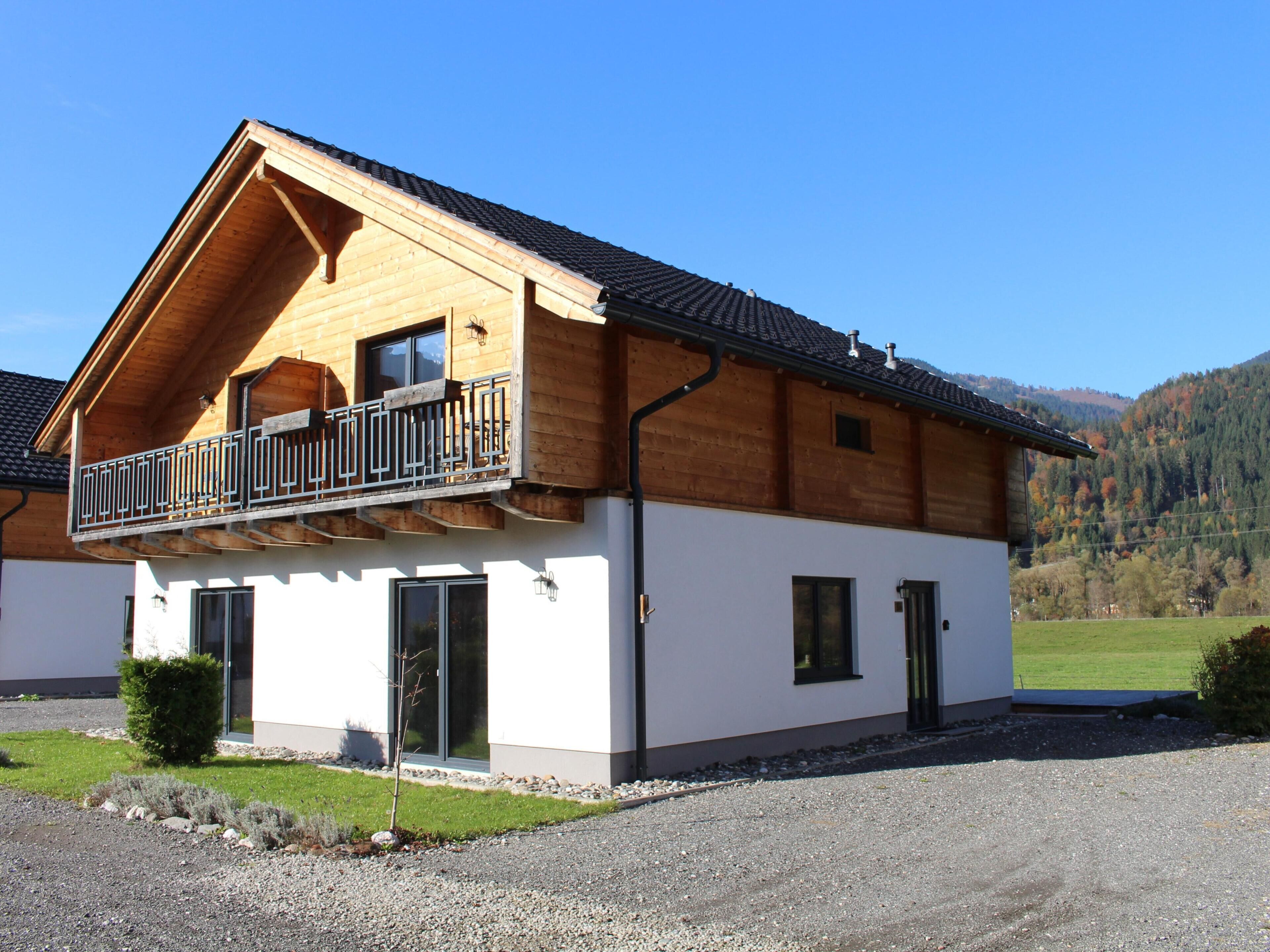 Ein zweistöckiges Holzhaus mit Balkon, großen Fenstern und einer Zuwegung mit Kies.
