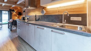 Une cuisine moderne avec des poutres en bois, un plan de travail en granit, un évier en acier inoxydable et un coin repas comprenant une table et des chaises.