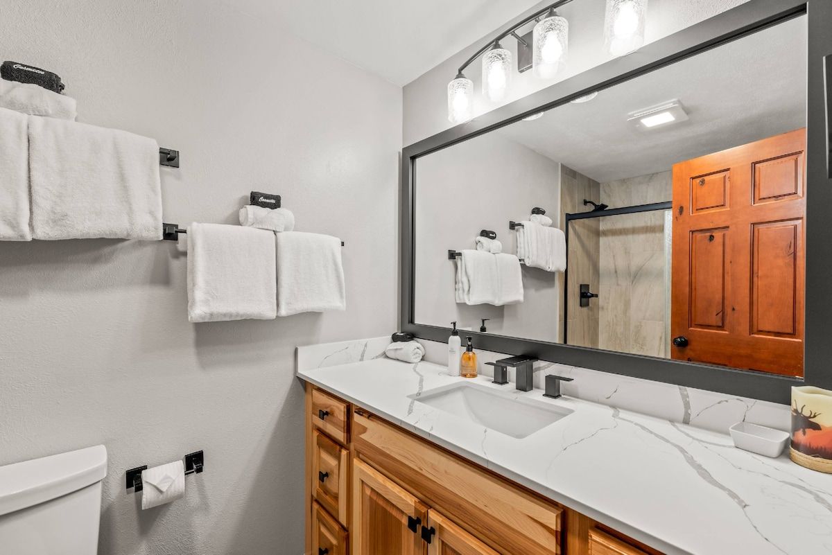 Une salle de bain avec un lavabo en marbre blanc, des meubles en bois, un grand miroir et des serviettes blanches.