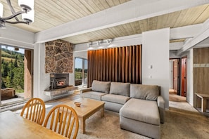 Een moderne woonkamer met een stenen openhaard, een hoekbank en een eethoek met een tafel en stoelen.