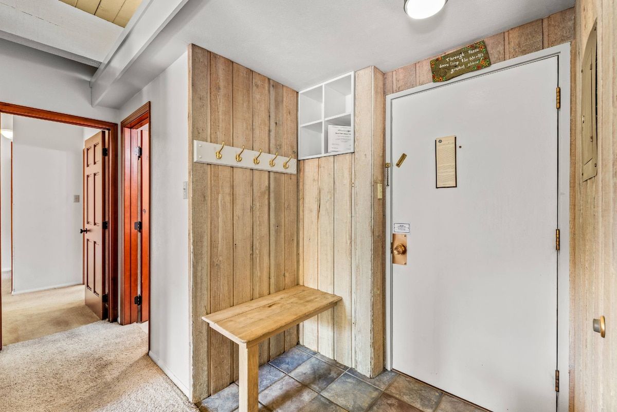 Un corridoio con una panchina in legno, un appendiabiti e una porta con un cartello.