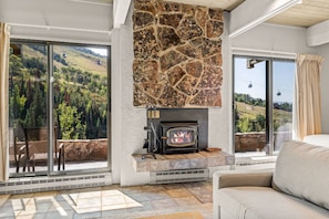 A cozy living room with a stone fireplace, large windows with scenic views, and comfortable seating.