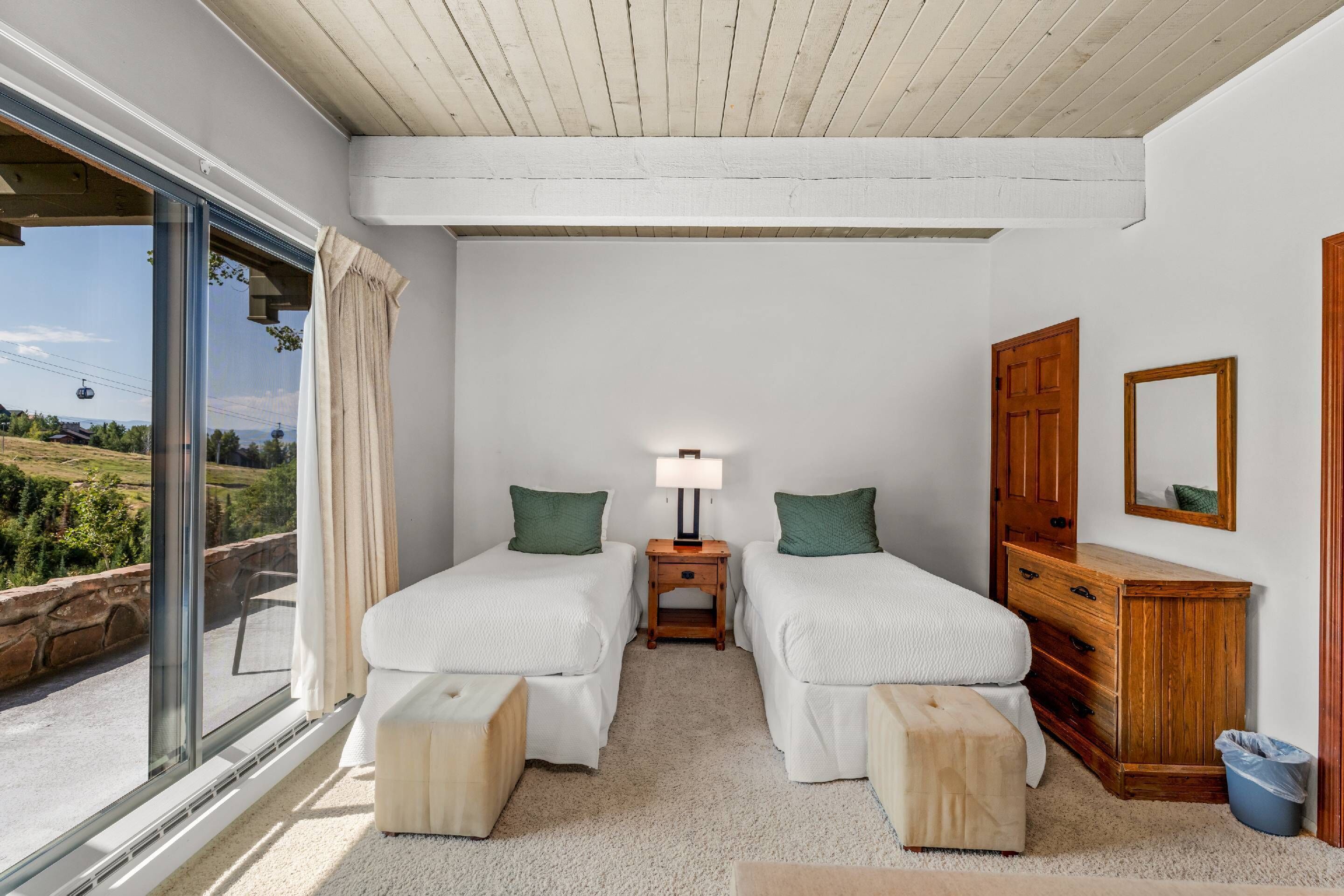 Un dormitorio con dos camas, un aparador de madera, un espejo y una ventana con vistas a zonas verdes.
